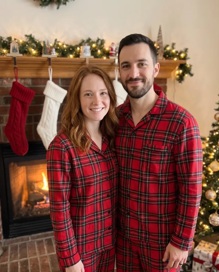 The same couple in matching red plaid pajamas by a fireplace with stockings