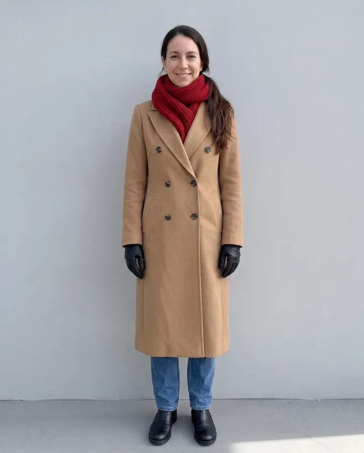 The same woman in a camel wool coat with a red scarf and black gloves