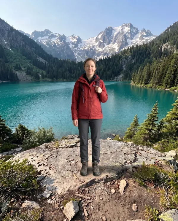 The hiker in the red jacket standing on the rock in front of the alpine lake