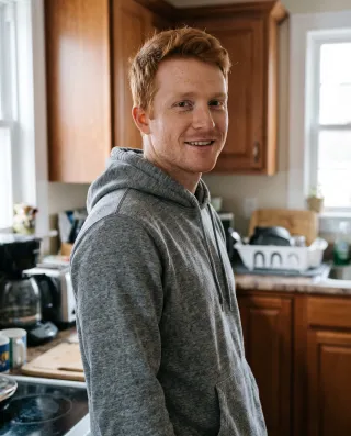 A man with red hair in a grey hoodie in his kitchen