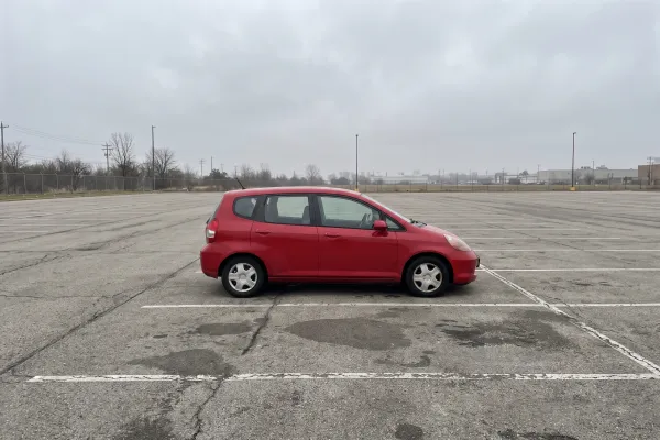 A red hatchback in an empty grey parking lot