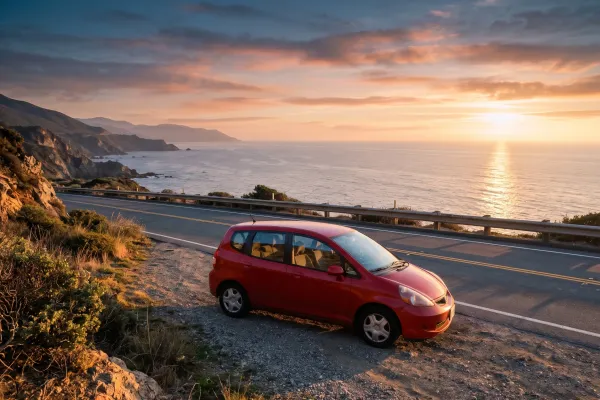The same red hatchback on a coastal road at sunset by the sea