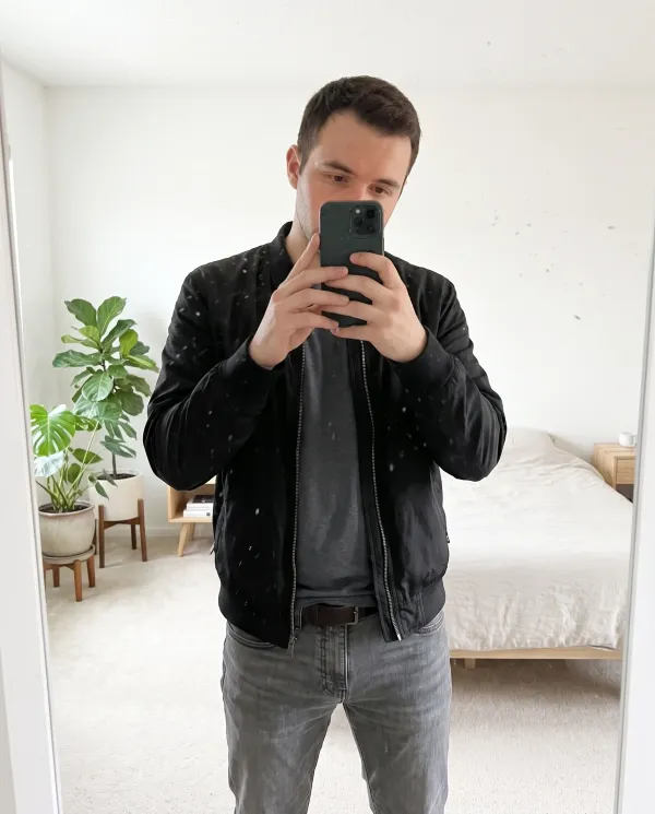 The same mirror selfie in a clean, bright room with a white wall and a plant