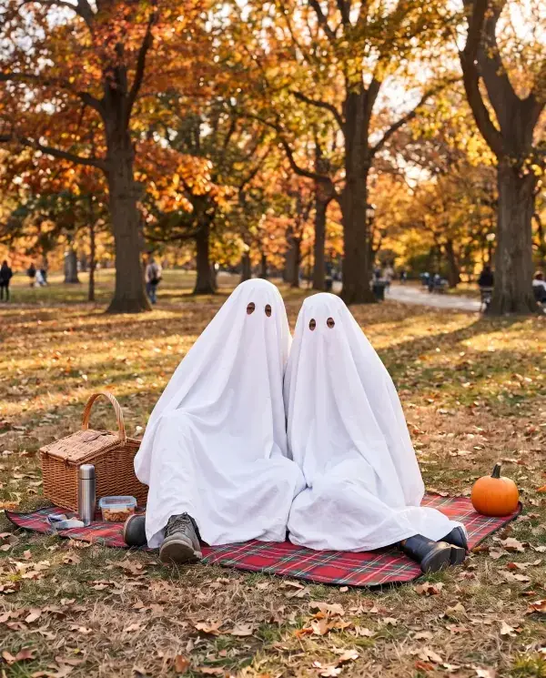 A couple as two sheet ghosts sitting on a picnic blanket in an autumn park