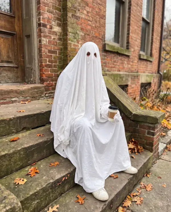 The man on the brick steps covered in a white sheet ghost costume, holding his coffee