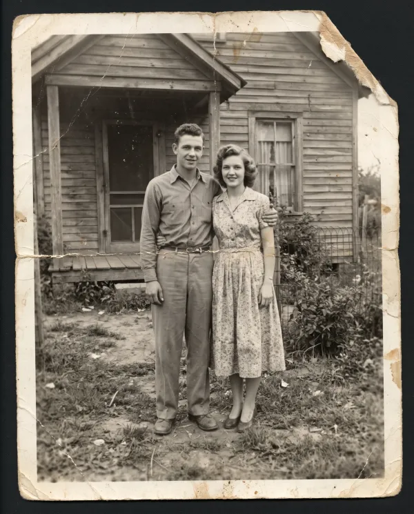 A scratched and stained black-and-white photo of a couple in front of a wooden house