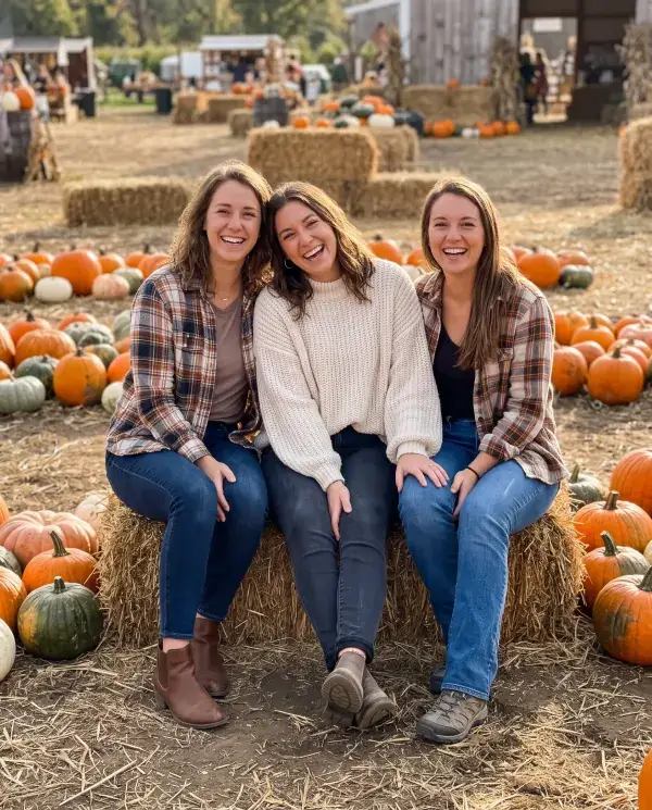 Three women friends sitting on hay bales at a pumpkin patch