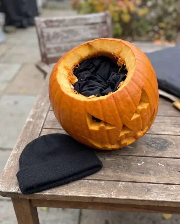 A carved pumpkin lined with black fabric inside, a black beanie beside it